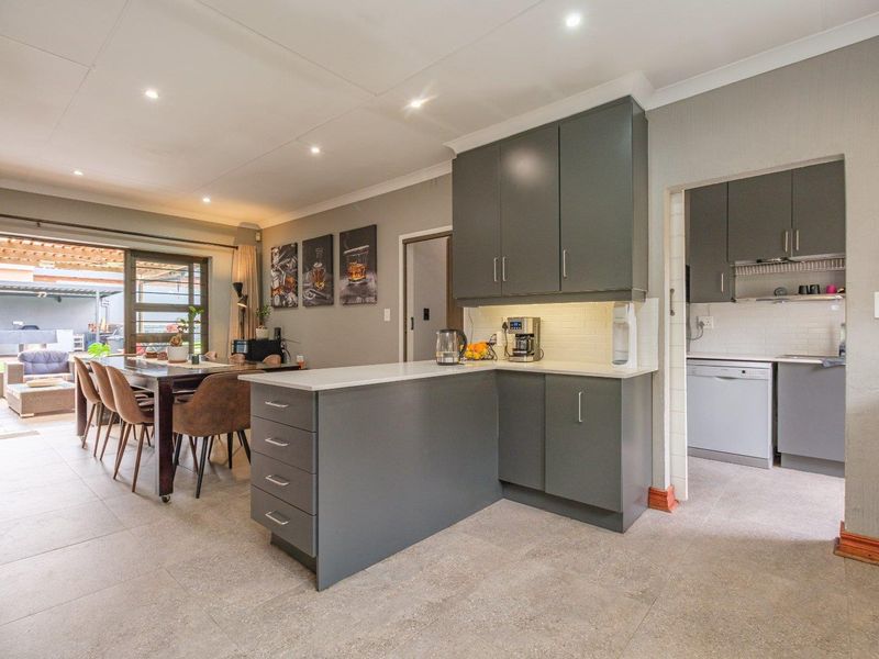 Open plan kitchen and dining area featuring modern grey cabinetry, stone countertops, recessed lighting, and seamless access to the outdoor patio.