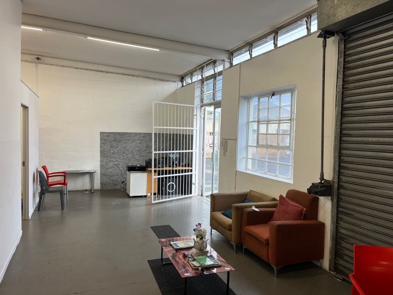 Open plan commercial space featuring industrial flooring, security gate, roller shutter door, and clerestory windows, suitable for various business or retail applications.