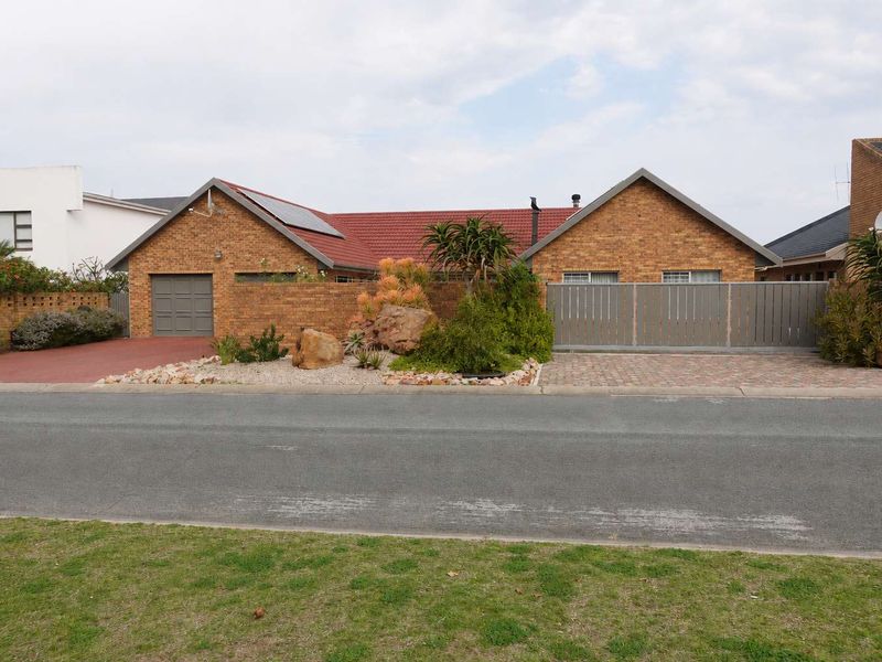 Front elevation of a single-story brick house featuring a tiled roof, solar panels, a garage, and a private gated driveway with landscaped garden.