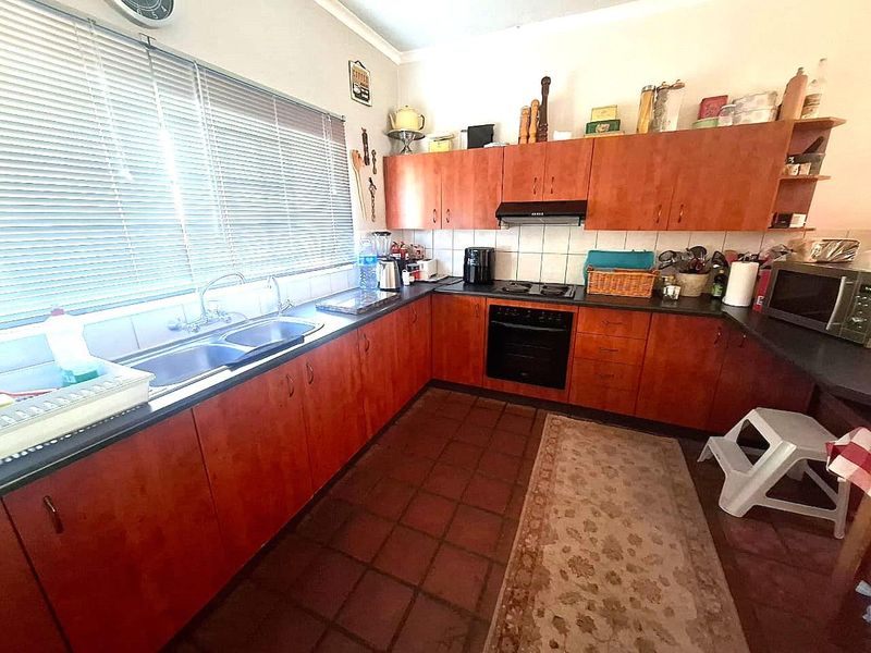 A functional kitchen featuring wooden cabinetry, a double basin sink, built-in oven, hob, extractor fan, and tiled flooring with a tiled backsplash.