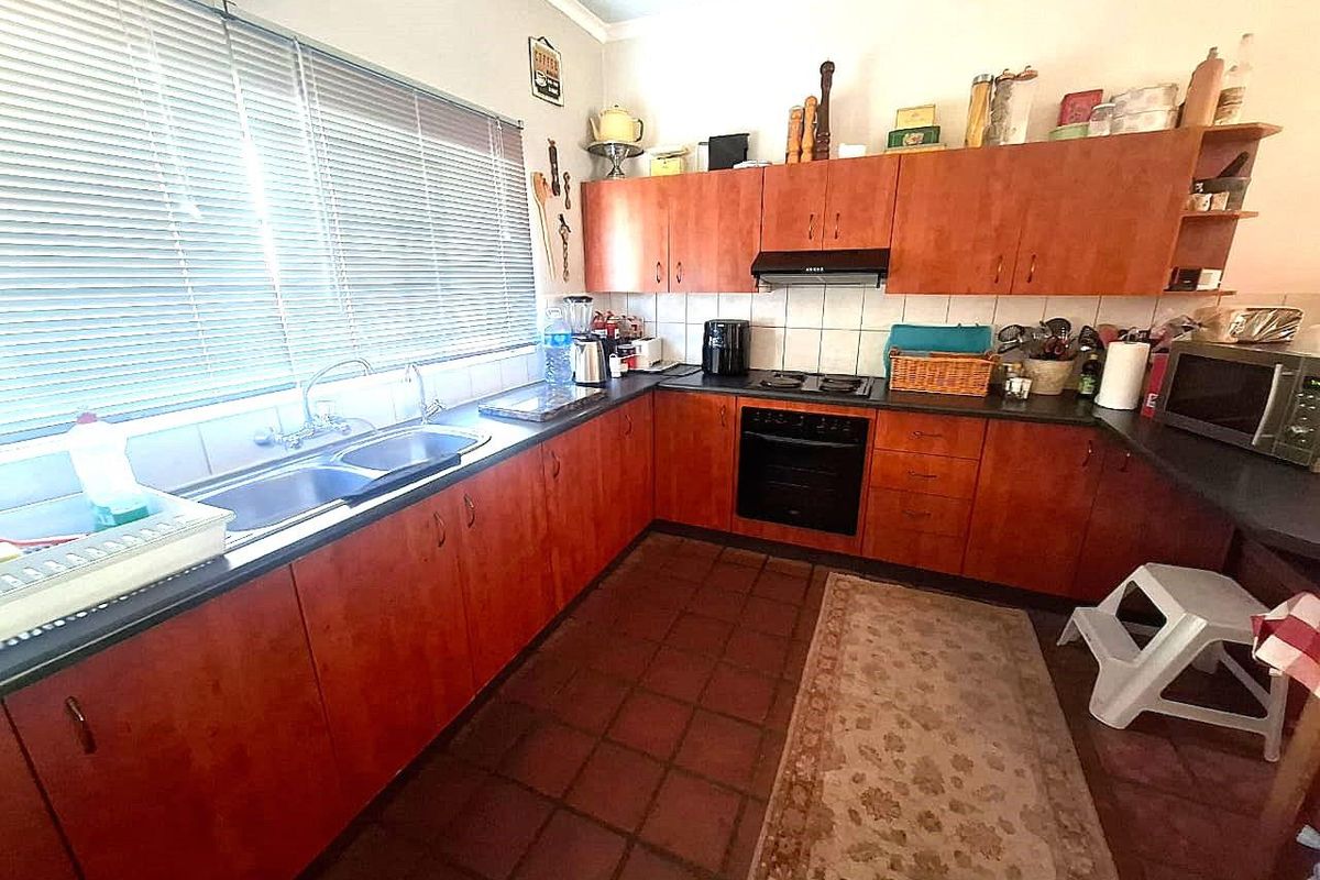 A functional kitchen featuring wooden cabinetry, a double basin sink, built-in oven, hob, extractor fan, and tiled flooring with a tiled backsplash.