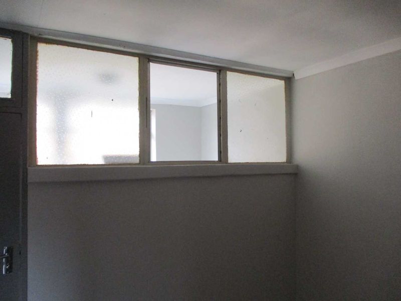 An empty bedroom interior featuring a high-level transom window providing natural light from an adjacent space, with neutral wall finishes.