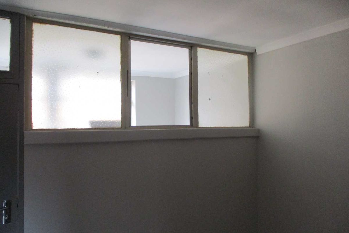 An empty bedroom interior featuring a high-level transom window providing natural light from an adjacent space, with neutral wall finishes.