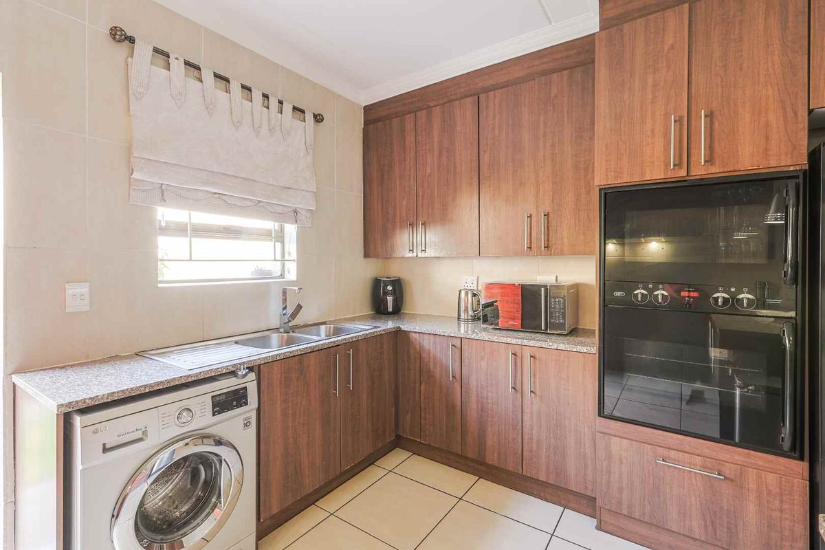 A functional kitchen featuring wood-look cabinetry, granite countertops, a double sink, and a built-in double oven with tiled flooring and backsplash.
