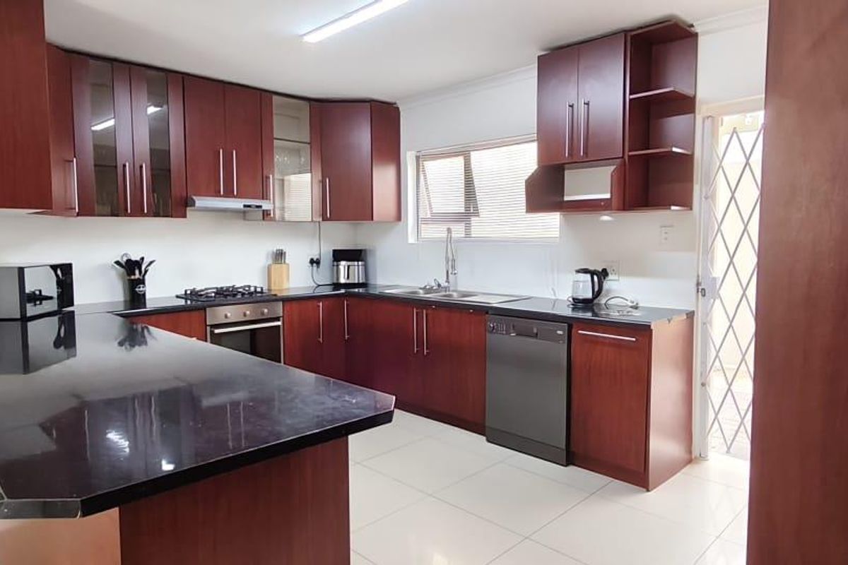 A functional kitchen featuring dark wood cabinetry, black countertops, a breakfast bar, gas hob, and tiled flooring with direct access to an exterior area.