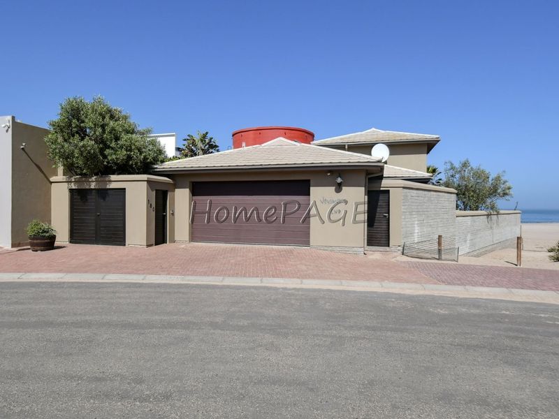 Front elevation of a coastal property featuring a double garage, paved driveway, and direct access to the beach area.