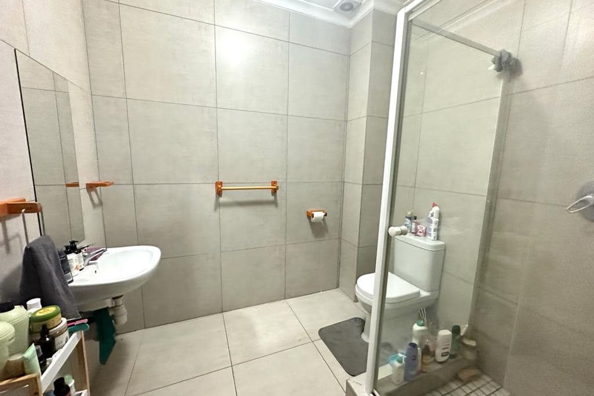 A modern bathroom featuring large-format wall and floor tiles, a glass-enclosed shower, a pedestal basin, and a toilet.