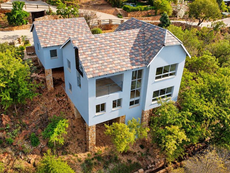 Aerial view of a multi-level house featuring a tiled roof, stone cladding, and a balcony, set within a natural, elevated landscape.