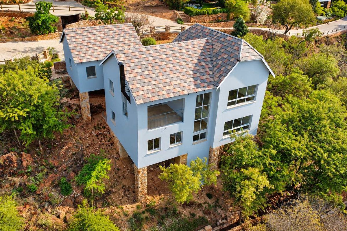 Aerial view of a multi-level house featuring a tiled roof, stone cladding, and a balcony, set within a natural, elevated landscape.
