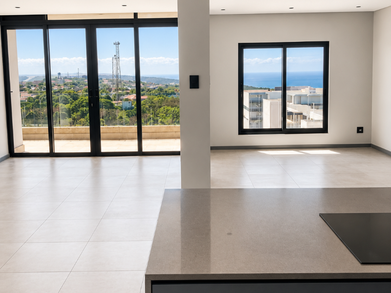 Spacious open-plan living area featuring a modern kitchen island with integrated hob, large sliding glass doors, and expansive coastal views.