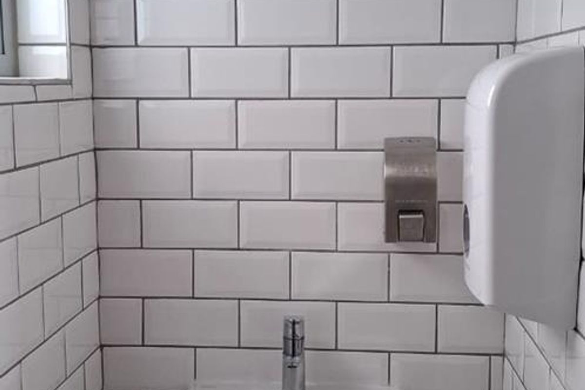 A clean, modern office restroom featuring white subway tile wall cladding, a wall-mounted basin with a chrome mixer tap, and wall-mounted dispensers.