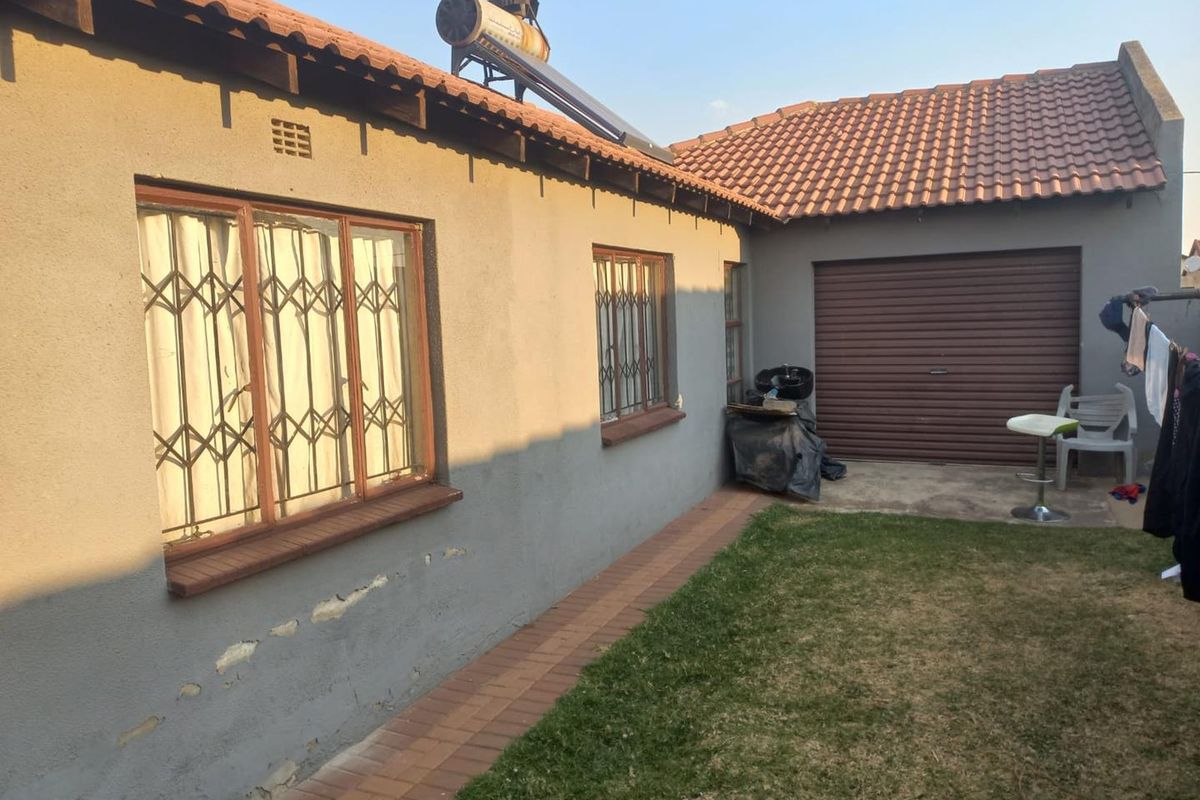 Rear view of the property featuring a tiled roof, solar water heater, security gates on windows, and a roller garage door.