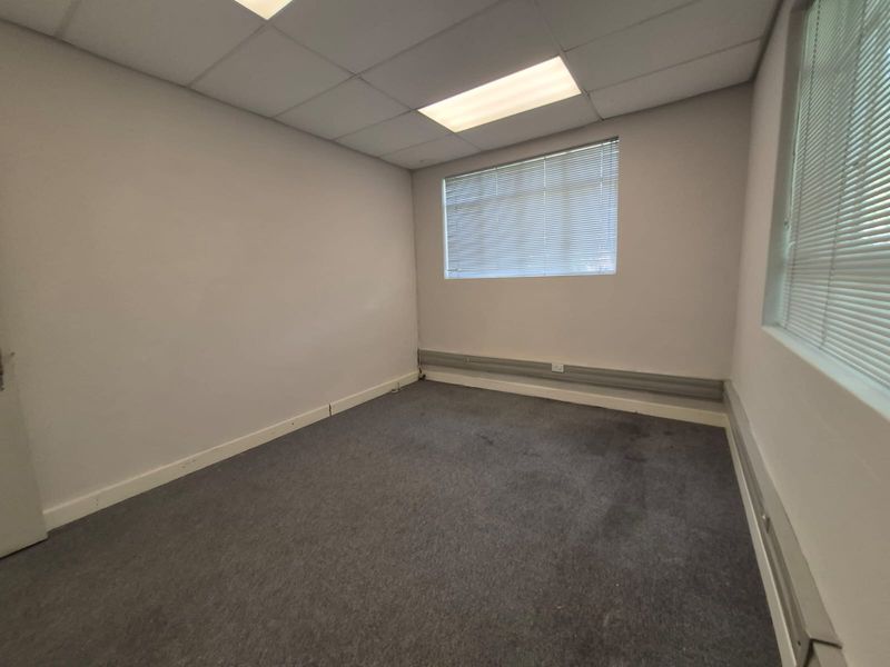 A vacant office space featuring a suspended ceiling, recessed lighting, window blinds, and surface-mounted electrical trunking along the walls.