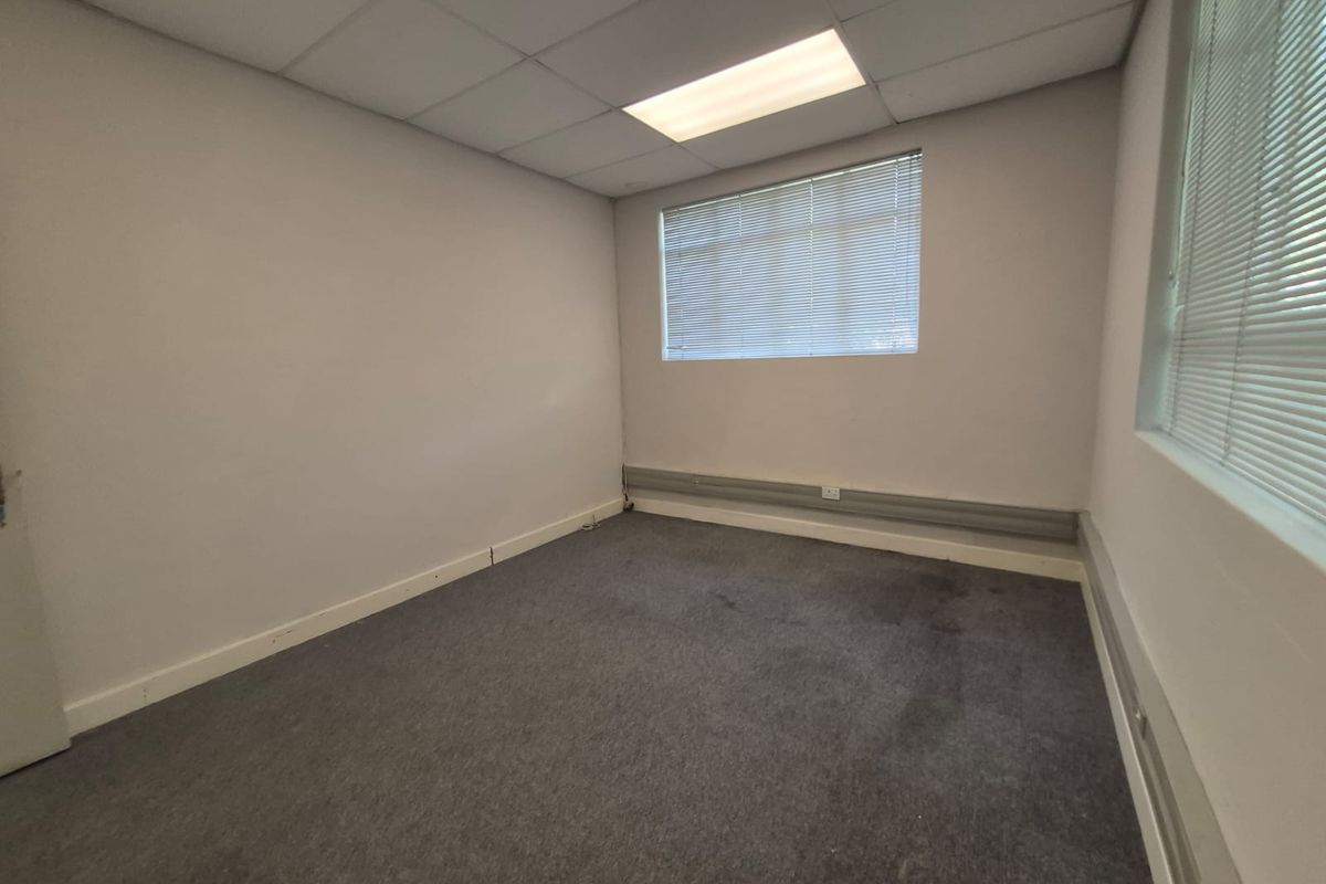 A vacant office space featuring a suspended ceiling, recessed lighting, window blinds, and surface-mounted electrical trunking along the walls.