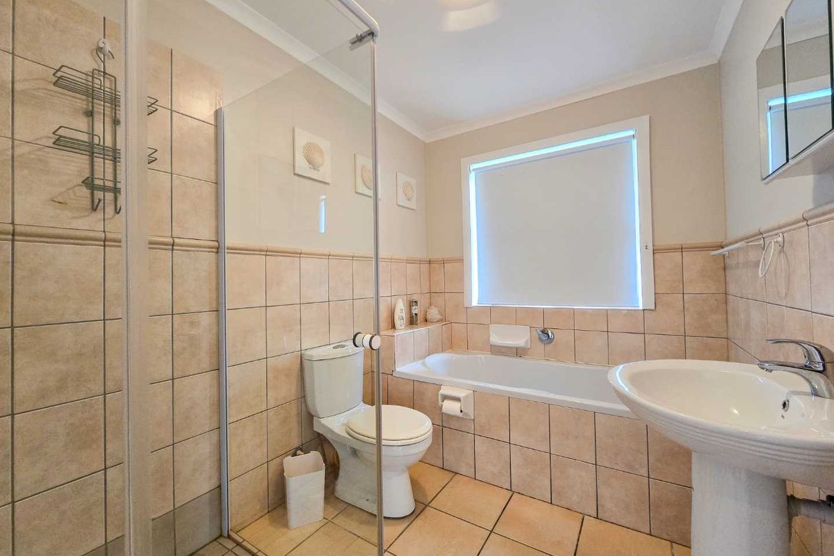 A functional bathroom featuring a pedestal sink, a built-in bathtub, and a separate glass-enclosed shower with neutral wall and floor tiling.