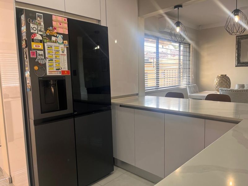 Modern kitchen featuring sleek white cabinetry, stone benchtops, and contemporary pendant lighting, seamlessly flowing into an adjacent dining area.