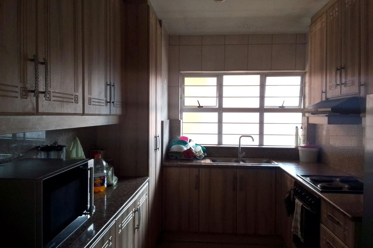 A functional galley-style kitchen featuring wood-finish cabinetry, laminate countertops, integrated oven and hob, and a window with security bars.