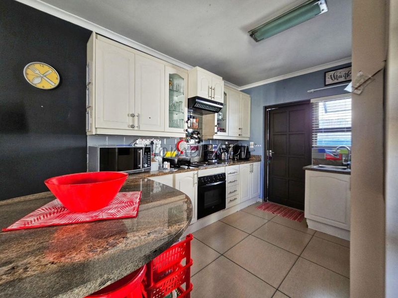 A functional kitchen featuring granite countertops, ample built-in cabinetry, an electric oven with extractor fan, and tiled flooring with direct exterior access.