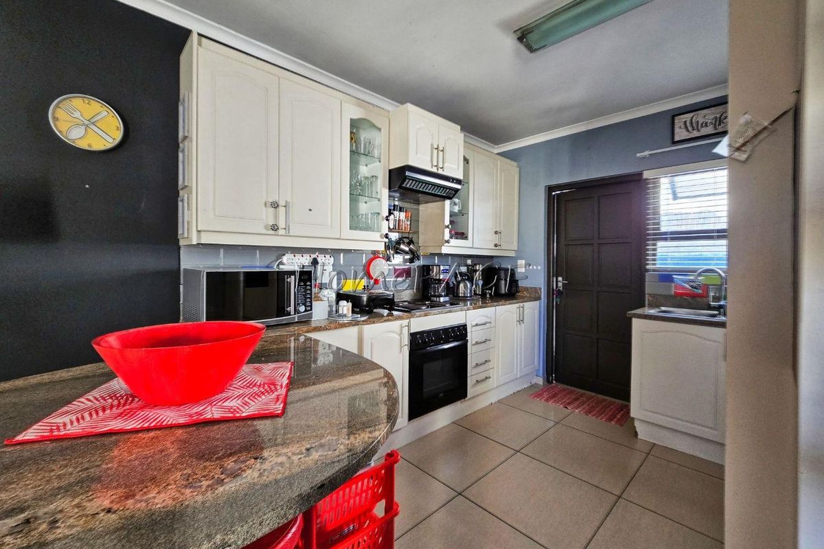 A functional kitchen featuring granite countertops, ample built-in cabinetry, an electric oven with extractor fan, and tiled flooring with direct exterior access.