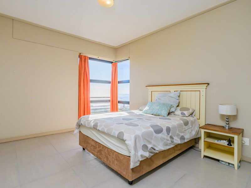 A bright bedroom featuring large corner windows with natural light and neutral tiled flooring, offering a clean and functional living space.