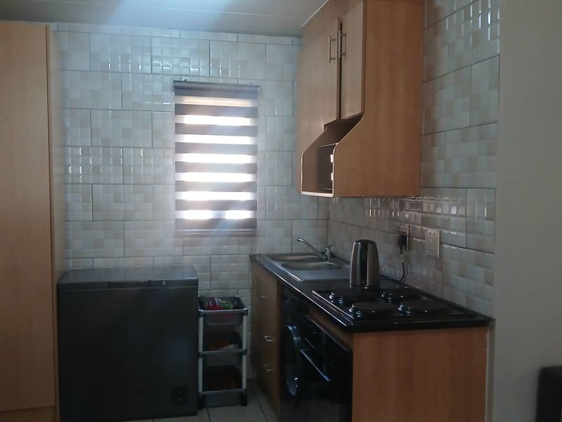 A functional kitchen featuring light wood-tone cabinetry, tiled backsplash, integrated hob and oven, and a stainless steel sink with a window view.