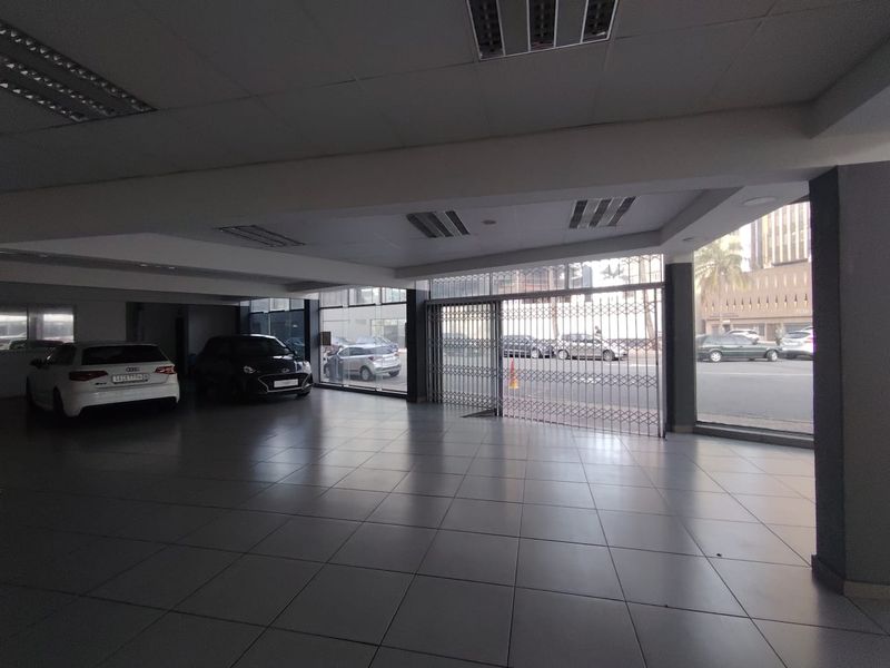 Spacious open-plan retail showroom featuring large glass storefront windows, tiled flooring, and recessed lighting, suitable for various commercial display purposes.