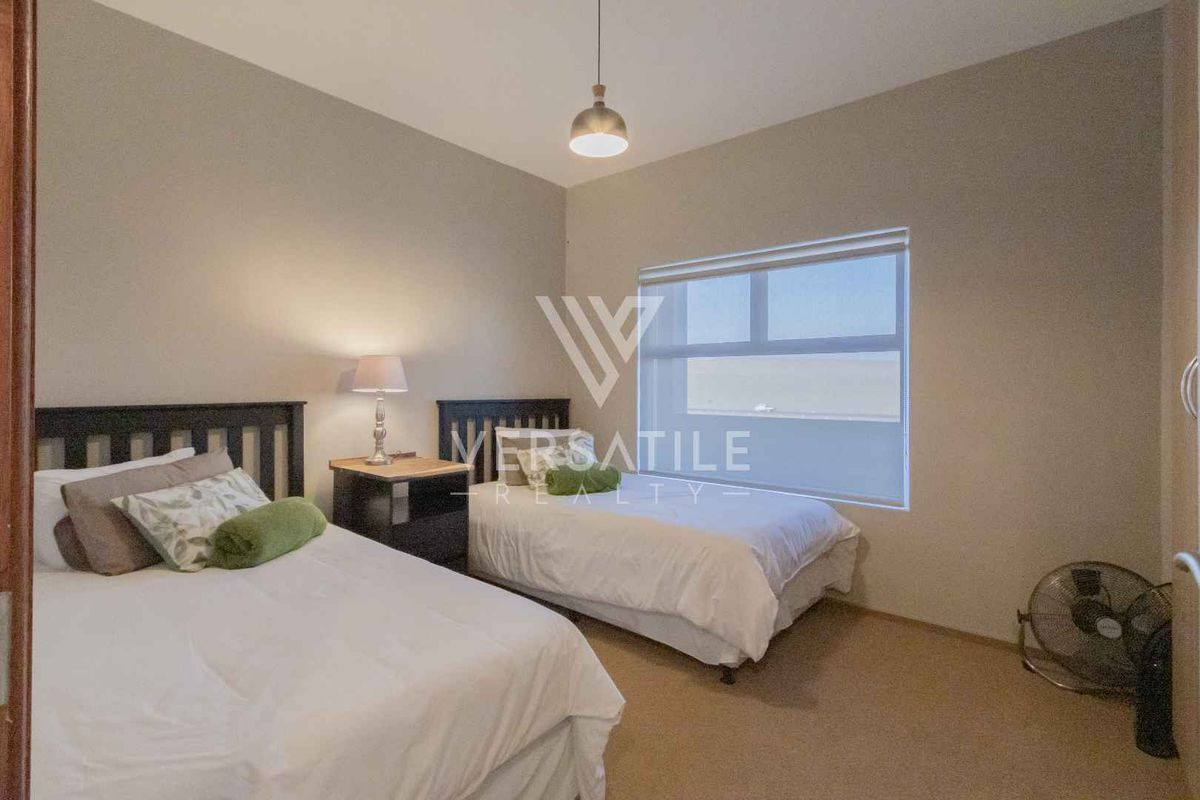 A well-maintained bedroom featuring neutral wall tones, carpeted flooring, and a large window with a roller blind for natural light.