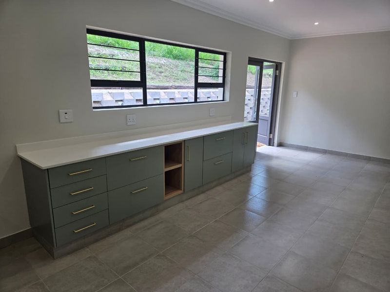 A modern, empty kitchen featuring sage green cabinetry, stone countertops, tiled floors, and direct access to the exterior through a glass door.