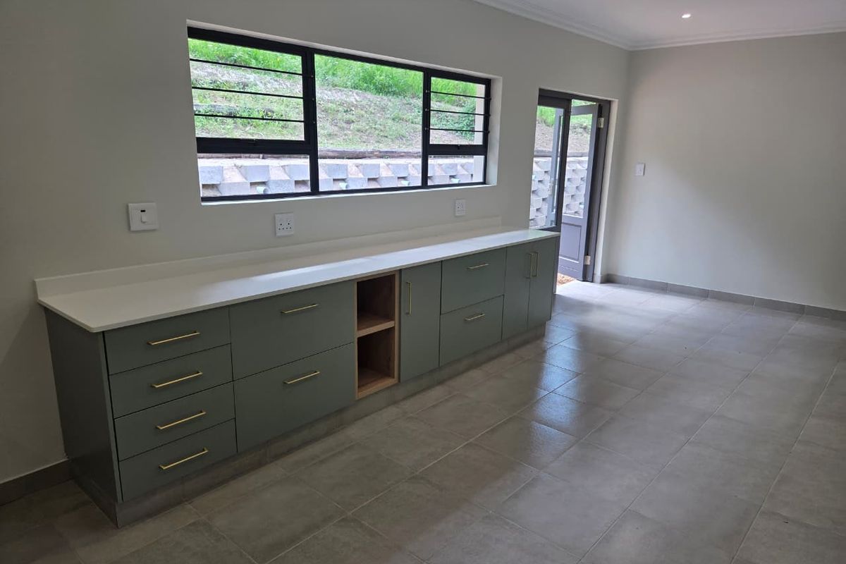 A modern, empty kitchen featuring sage green cabinetry, stone countertops, tiled floors, and direct access to the exterior through a glass door.