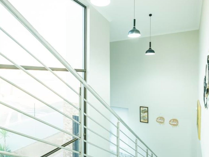 Bright and modern hallway featuring a staircase with a sleek metal balustrade, large window for natural light, and contemporary pendant lighting.