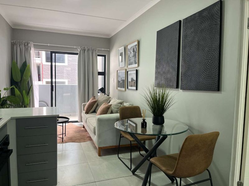 A modern open-plan living and dining area featuring tiled floors, neutral wall tones, and a sliding glass door leading to an outdoor balcony space.