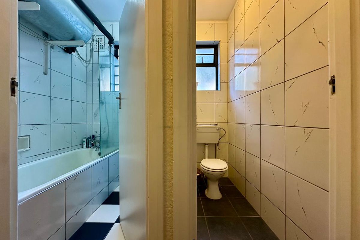 A split-view bathroom featuring a tiled bathtub area with a glass screen and a separate toilet compartment with matching wall tiles.