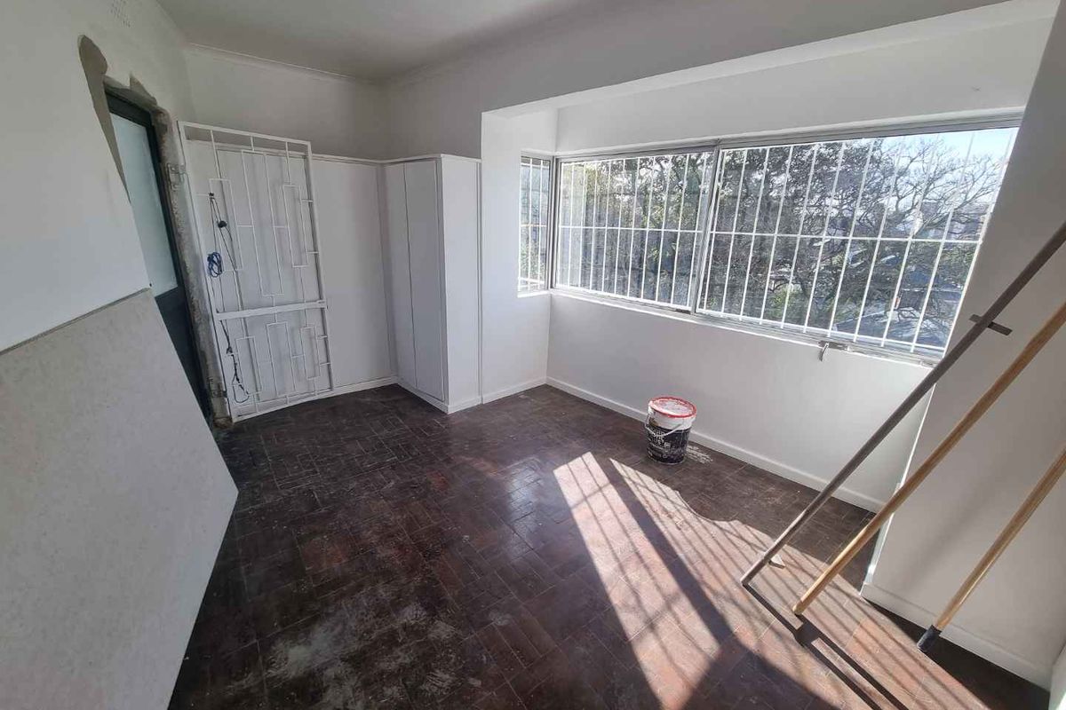 An empty bedroom undergoing renovation, featuring parquet flooring, built-in cupboards, and security bars on the windows.