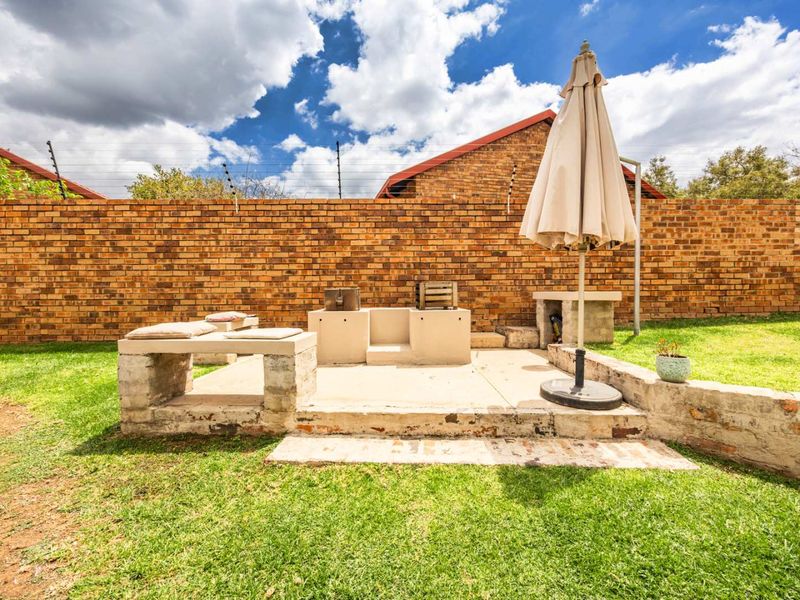 Rear garden area featuring a built-in braai, concrete patio space, and a high brick boundary wall with electric fencing.