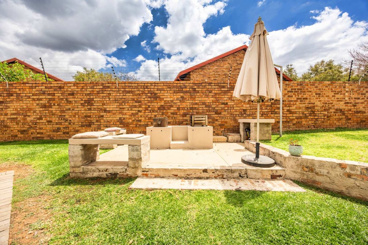 Rear garden area featuring a built-in braai, concrete patio space, and a high brick boundary wall with electric fencing.