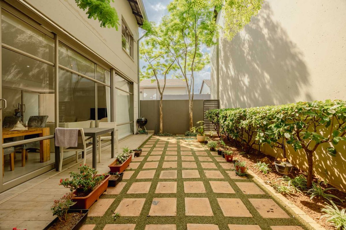 A well-maintained rear courtyard featuring a paved patio area, landscaped garden beds, and large sliding glass doors providing seamless indoor-outdoor flow.