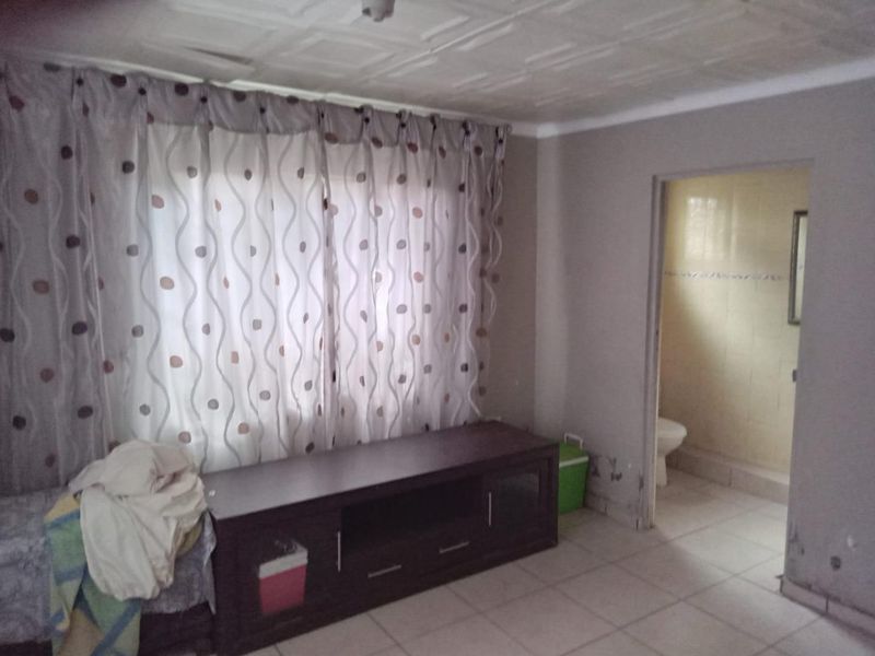 Living room area with tiled flooring and textured ceiling, featuring an adjacent bathroom with tiled walls and visible wall surface wear.