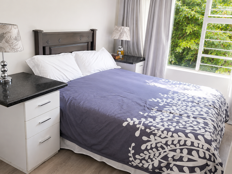 A well-lit bedroom featuring built-in bedside cabinets with granite tops, laminate flooring, and a large window overlooking greenery.