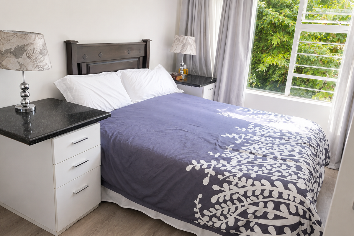 A well-lit bedroom featuring built-in bedside cabinets with granite tops, laminate flooring, and a large window overlooking greenery.