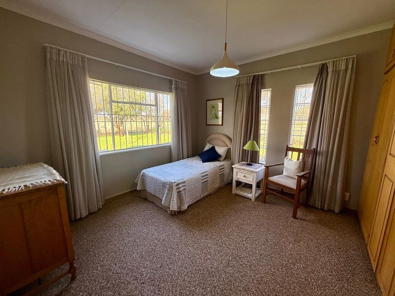 A well-lit bedroom featuring carpeted flooring, built-in wardrobe storage, and large windows with security bars overlooking the farm grounds.
