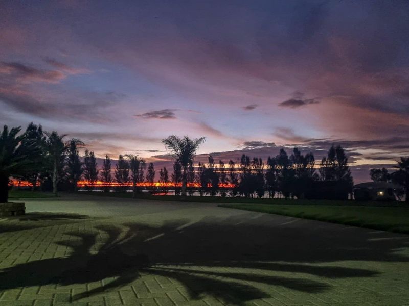 A scenic view of the property grounds at sunset, featuring a paved driveway and mature trees against a dramatic evening sky.