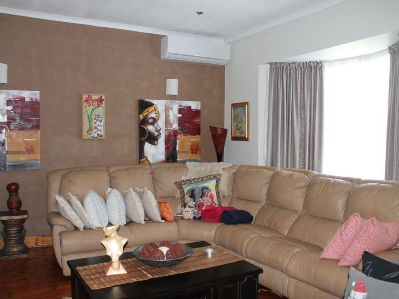 A comfortable living room featuring timber flooring, a bay window, and a wall-mounted split-system air conditioner.