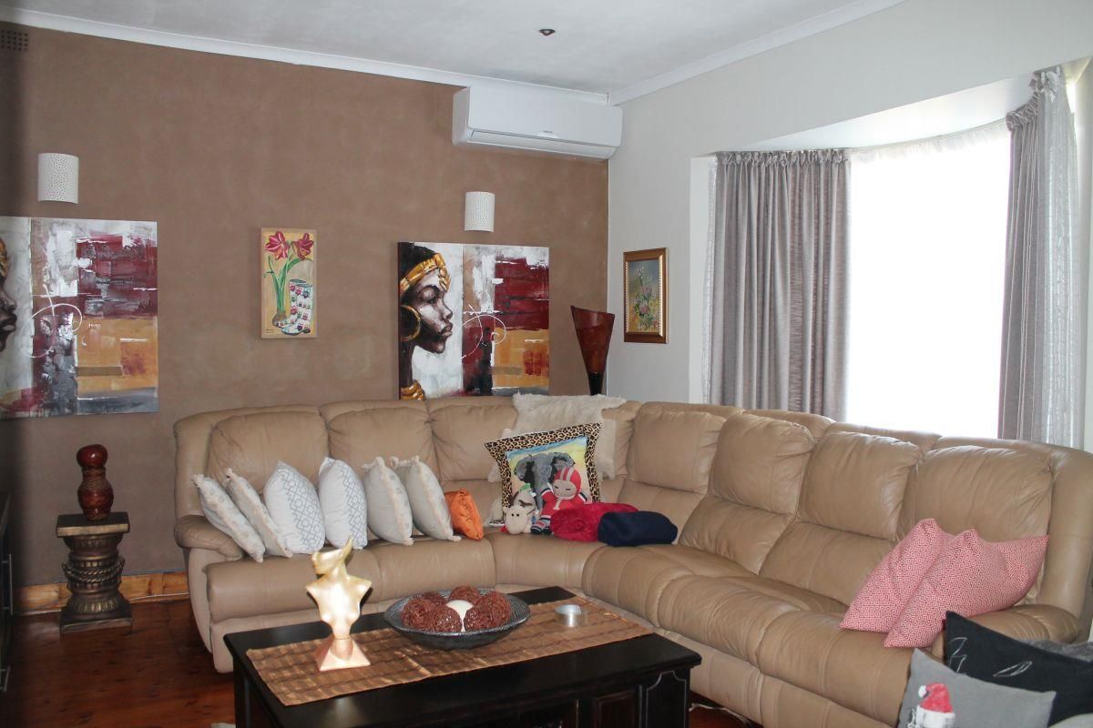 A comfortable living room featuring timber flooring, a bay window, and a wall-mounted split-system air conditioner.