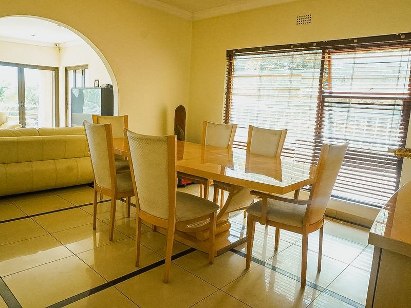 A dining room featuring tiled flooring, a decorative archway leading to an adjacent living area, and large windows fitted with venetian blinds.