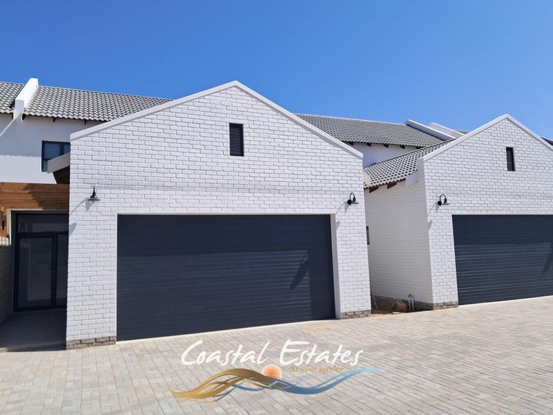 Modern townhouse exterior featuring white brick facades, dark grey garage doors, and a neatly paved driveway under a clear blue sky.