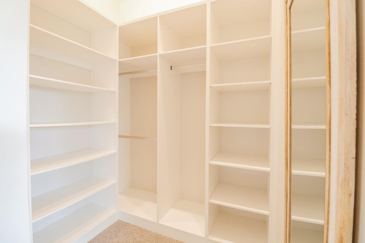 A walk-in closet featuring extensive built-in white shelving and hanging rails, providing ample organized storage space.