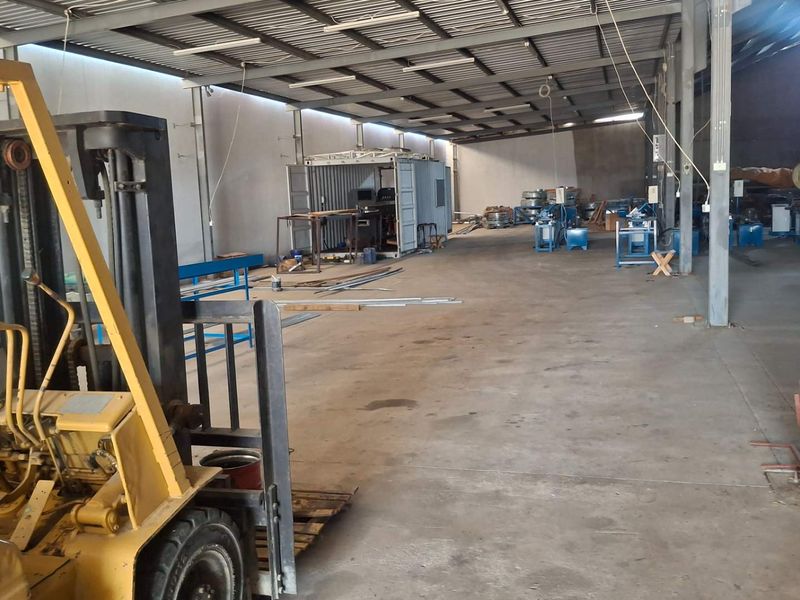 Spacious industrial warehouse area featuring exposed steel roof trusses, concrete flooring, and steel support columns, suitable for manufacturing or storage operations.