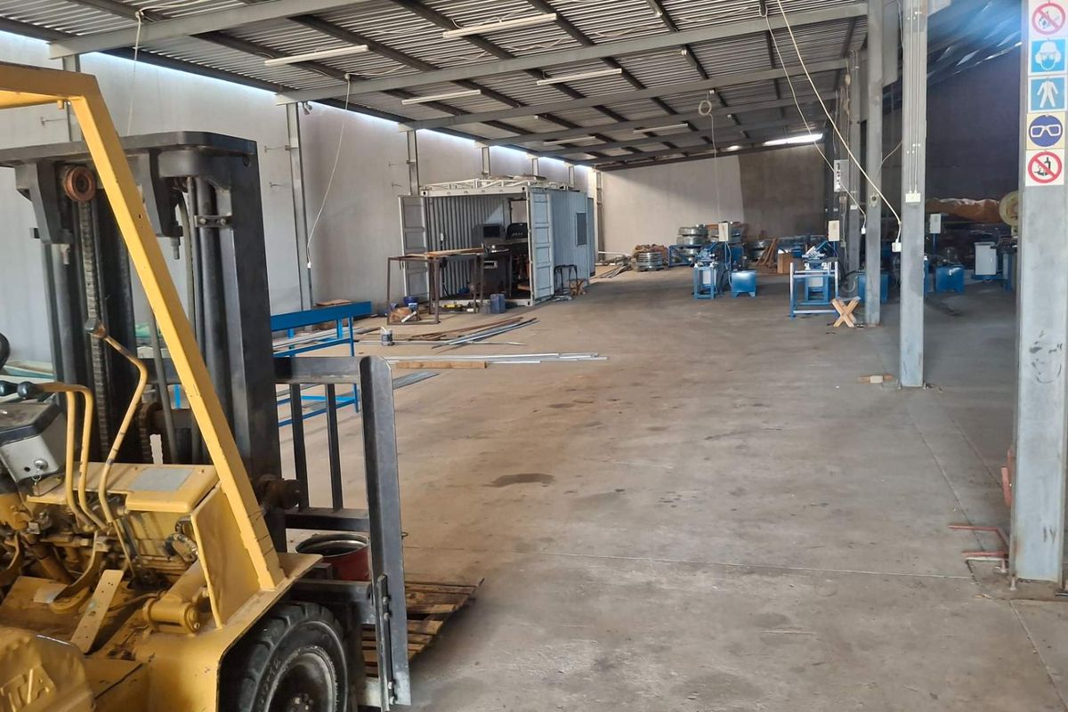 Spacious industrial warehouse area featuring exposed steel roof trusses, concrete flooring, and steel support columns, suitable for manufacturing or storage operations.