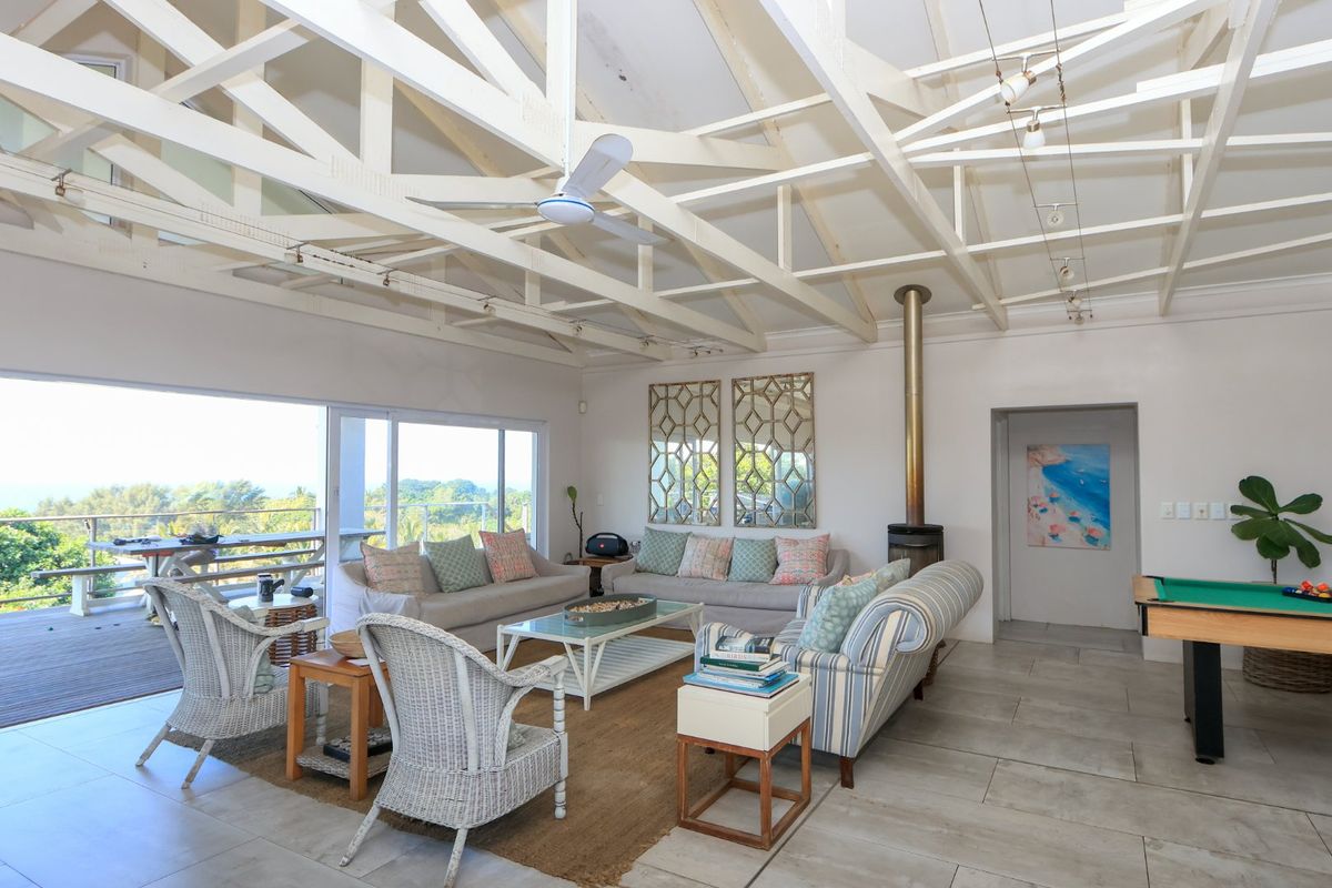 Spacious living area featuring high exposed timber trusses, a freestanding fireplace, and large sliding doors opening onto an outdoor deck with scenic views.