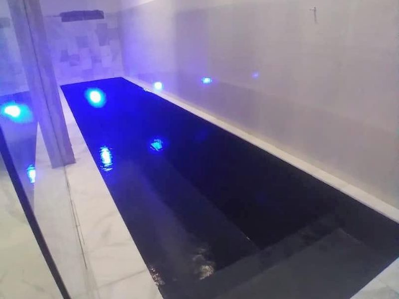 An indoor swimming pool area featuring modern tiled flooring, recessed lighting, and high-level windows, creating a sleek and contemporary aquatic space.